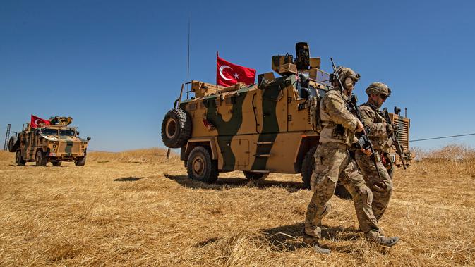 Pasukan AS berjalan melewati kendaraan militer Turki saat patroli gabungan di Desa al-Hashisha, Tal Abyad, Suriah, Minggu (8/9/2019). AS dan Turki patroli gabungan di Suriah timur laut untuk meredakan ketegangan Ankara dengan pasukan Kurdi yang didukung AS dalam memerangi ISIS. (DELIL SOULEIMAN/AFP)