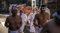 Penganut Shinto berlari saat melakukan pemanasan sebelum mandi dengan air dingin di Kuil Teppozu Inari, Tokyo, Jepang, 8 Januari 2023. Ritual Tahun Baru ini dilakukan untuk memurnikan jiwa dan raga. (Philip FONG/AFP)
