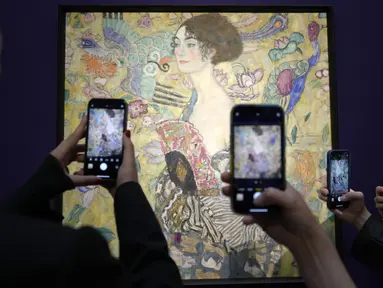 Orang-orang memotret 'Dame mit Faecher' (Lady with a Fan) karya Gustav Klimt saat dipajang di ruang lelang Sotheby's di London, Selasa (20/6/2023). (AP Photo/Kirsty Wigglesworth)