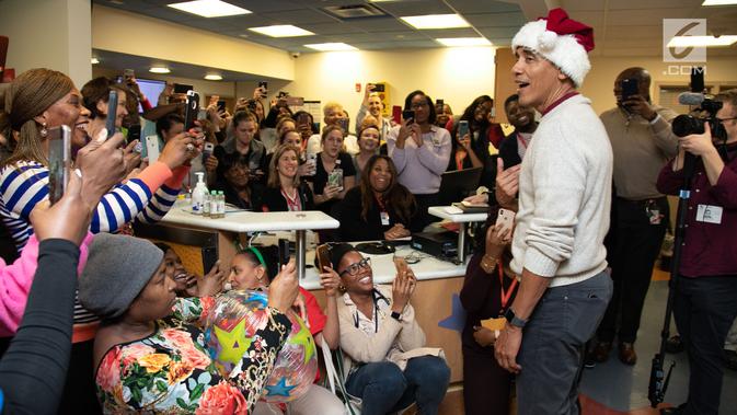Mantan Presiden AS, Barack Obama mengunjungi Children's National Medical Center di Washington, Rabu (19/12). Dengan topi khas merah putih ala sinterklas, Obama membagikan hadiah natal untuk anak-anak yang sedang menjalani perawatan. (Chuck Kennedy / AFP)