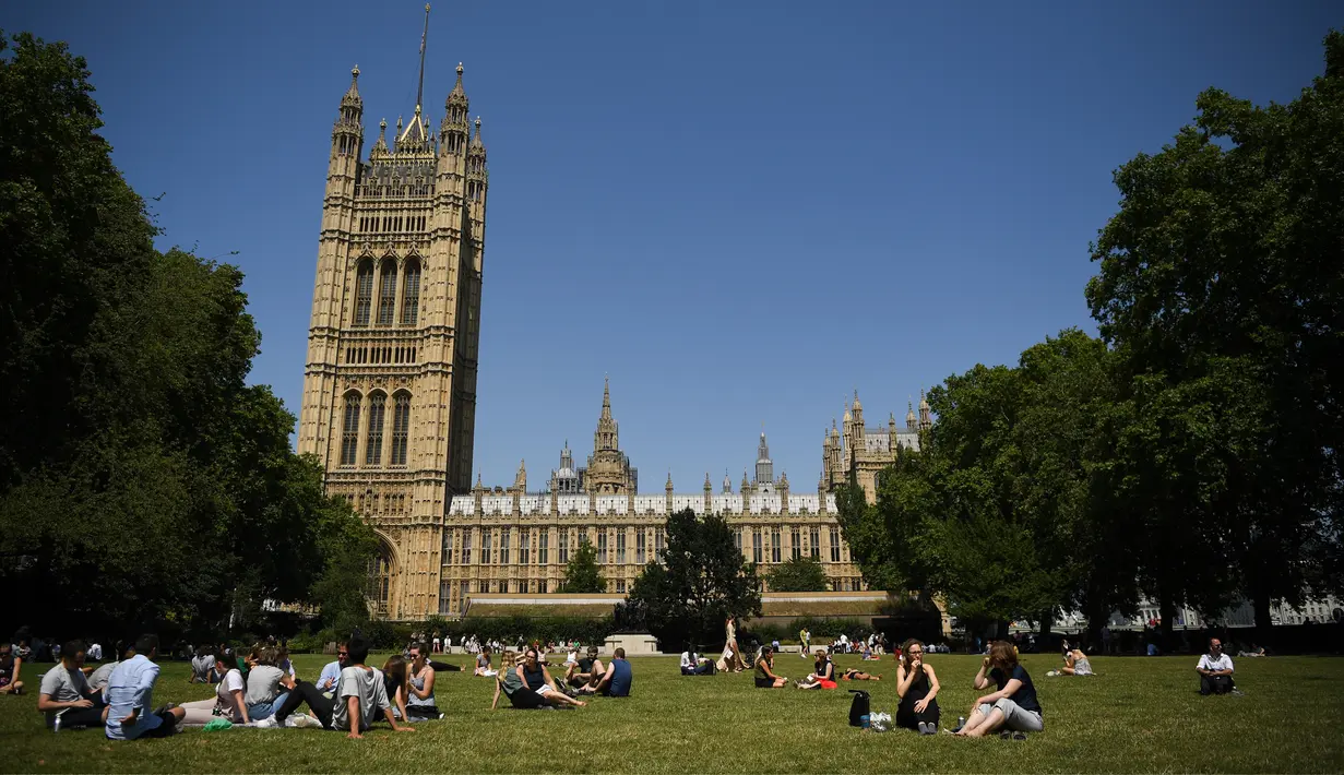 Orang-orang berbincang saat bersantai di bawah sinar matahari di Victoria Tower Gardens dekat Gedung Parlemen di London (23/7/2019). Suhu melonjak di atas 30C (86F) di Inggris pada 23 Juli dengan para peramal cuaca memperkirakan suhu setinggi 37C (96.8F) sebelum akhir pekan. (AFP Photo/Ben Stansall)