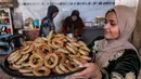 Kue ini sering dianggap sebagai camilan khas. Tampak dalam foto, seorang wanita memegang nampan berisi biskuit tradisional "kaak" yang berbentuk cincin dan baru dipanggang menjelang Idul Fitri, hari raya yang menandai berakhirnya bulan puasa suci Ramadhan, di Kota Gaza pada 16 Maret 2026. (Omar AL-QATTAA/AFP)
