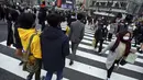 Orang-orang yang mengenakan masker berjalan di sepanjang penyeberangan pejalan kaki di daerah Shibuya, Tokyo, Selasa (5/1/2021). Ibu kota Jepang, Tokyo mengonfirmasi lebih dari 1.200 kasus virus corona COVID-19 baru pada Selasa (5/1). (AP Photo/Eugene Hoshiko)