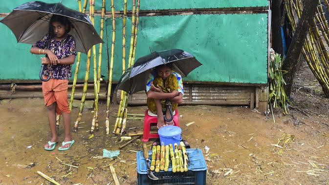 Dua anak perempuan pengungsi Rohingyah menjual tebu musim hujan di kamp pengungsi Kutupalong di Ukhia (12/9/2019). Kamp ini adalah salah satu dari dua kamp pengungsi yang dikelola pemerintah di Cox's Bazar, kamp yang satunya lagi adalah kamp pengungsi Nayapara. (AFP Photo/Munir Uz Zaman)