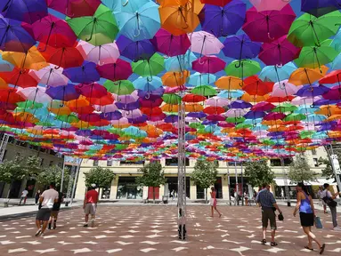 Pengunjung melewati instalasi Umbrella Sky Project di Aix-en-Provence, Prancis, Jumat (28/6/2019). Spot berteduh yang instagramable tersebut merupakan karya seniman Portugis Patricia Cunha. (BORIS HORVAT/AFP)