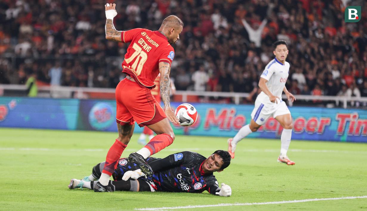 Kiper Arema FC, Adi Satryo (bawah) berhasil menghalau tendangan Gustavo Almeida saat pertandingan Persija Jakarta vs Arema FC BRI Super League pekan ke-20 yang berlangsung di Stadion Utama Gelora Bung Karno, Minggu (8/2/2026) malam WIB. (Bola.com/Abdul Aziz)