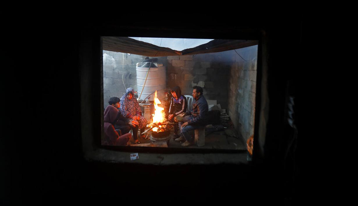 Sebuah keluarga duduk sekitar kayu bakar perapian rumah mereka saat cuaca dingin di daerah kumuh Kota Gaza, Palestina, 27 Januari 2022. (AP Photo/Hatem Moussa)