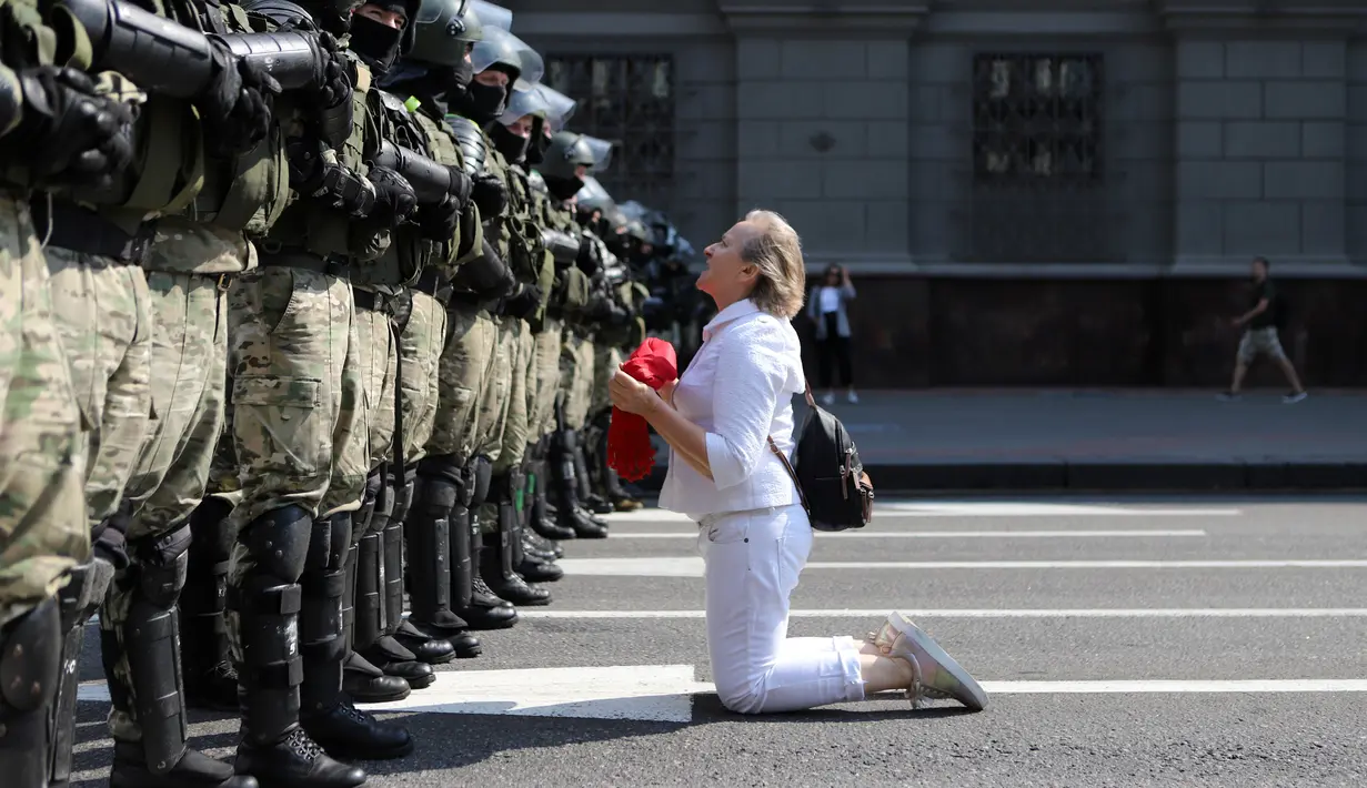 Seorang wanita berlutut di depan barisan polisi antihuru-hara saat mereka memblokir demonstrasi pendukung oposisi Belarusia di Minsk, Belarusia, Minggu (30/8/2020). Puluhan ribu demonstran berkumpul untuk menuntut agar Presiden Belarusia Alexander Lukashenko mengundurkan diri. (AP Photo)