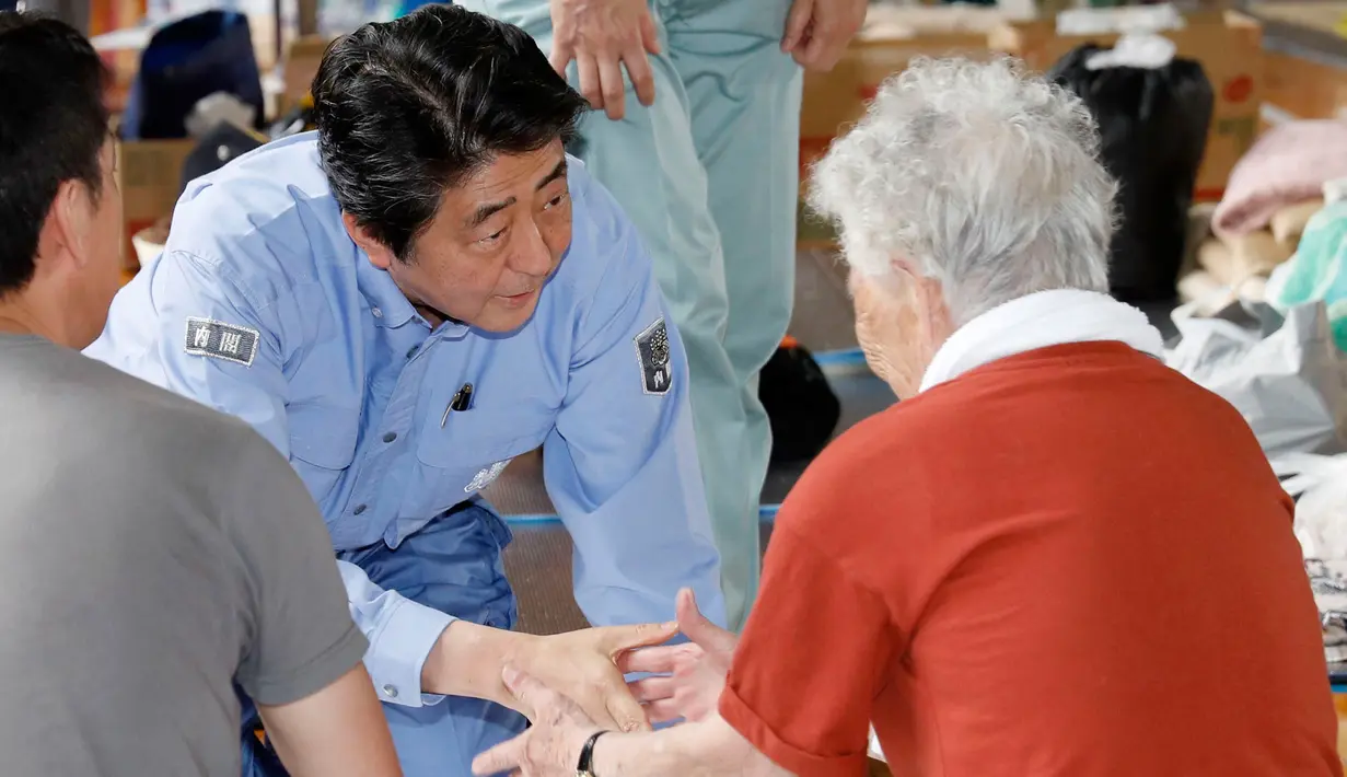 PM Jepang, Shinzo Abe berbincang dengan warga korban banjir saat mengunjungi lokasi penampungan di Kurashiki, Prefektur Okayama, Rabu (11/7). Korban tewas akibat bencana banjir di Jepang meningkat menjadi 179 jiwa. (Shohei Miyano/Kyodo News via AP)