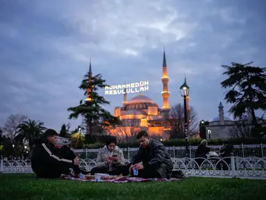Orang-orang berbuka puasa selama bulan suci Ramadhan, di luar masjid Sultanahmet berlatar tulisan dalam bahasa Turki "Muhammad adalah utusan Allah", Istanbul, Turki, Rabu 25 Februari 2026. Sepanjang Ramadan, Masjid Sultanahmet di Istanbul, Turki, selalau ramai dikunjungi. (AP Photo/Emrah Gurel)