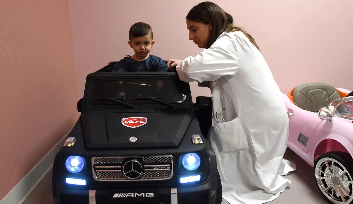 Petugas medis membantu Souvail (2) duduk di mobil mainan listrik menuju ruang operasi di Rumah Sakit Valenciennes, Prancis, Jumat (2/2). Program ini untuk membuat anak-anak lebih santai sebelum menjalani prosedur operasi. (FRANCOIS LO PRESTI/AFP)