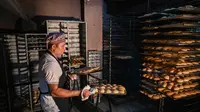 Foto yang diambil pada 20 Juli 2022 ini menunjukkan seorang tukang roti membawa nampan berisi roti bernama 'pandesal' di sebuah toko roti di Manila. (JAM STA ROSA / AFP)
