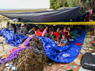 Pengungsi Rohingya berkumpul dalam tenda di pantai di Pulau Sabang, Provinsi Aceh, Indonesia, Minggu (3/12/2023). Lebih dari 100 pengungsi Rohingya, termasuk perempuan dan anak-anak, mendarat di pantai Aceh pada tanggal 2 Desember 2023 dini hari. (CHAIDEER MAHYUDDIN/AFP)