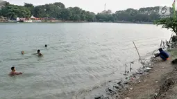 Anak-anak berenang dekat pemancing di Danau Sunter, Jakarta, Selasa (23/7/2019). Anak-anak tetap nekat berenang di Danau Sunter kendati mereka sadar telah dilarang dan dapat membahayakan diri sendiri. (merdeka.com/Iqbal Nugroho)