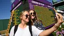Dua wanita berselfie di sebelah papan Order of Play pada hari ketiga Kejuaraan Tenis Wimbledon 2017 di The All England Lawn Tennis Club di Wimbledon, London barat daya, Inggris (5/7). (AFP Photo/Justin Tallis)