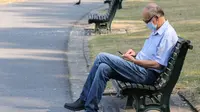 Seorang pria yang memakai masker duduk di bangku taman di Brussel, (12/8/2020). Penggunaan masker menjadi wajib di tempat umum di Brussel karena kasus Covid-19 naik ke tingkat kewaspadaan yang menempatkan kota itu di antara yang paling parah terkena dampak corona di Eropa. (François WALSCHAERTS/AFP)