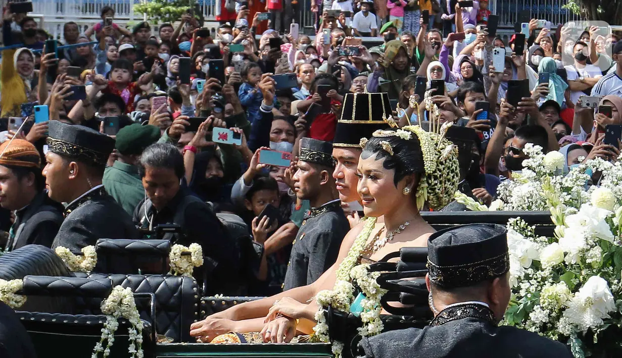 Pasangan pengantin Kaesang Pangarep dan Erina Gudono menaiki kereta saat prosesi kirab Ngunduh Mantu di kawasan Selamet Riyadi, Solo, Jawa Tengah, Minggu (11/12/2022). Kirab ngunduh mantu pernikahan putra bungsu Presiden Joko Widodo, Kaesang Pangarep dan istrinya Erina Gudono yang dimulai dari Loji Gandrung menuju Pura Mangkunegaran tersebut disaksikan ribuan masyarakat Solo dan sekitarnya. (Liputan6.com/Herman Zakharia)