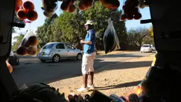 Seorang pria menjual buah-buahan dan sayuran di dalam bagasi mobil di sisi jalan yang sibuk di Harare, 7 Juli 2020. Mobil menjadi pasar bergerak di mana penduduk Zimbabwe menjual barang dagangan dari kendaraan untuk mengatasi kesulitan ekonomi yang disebabkan Covid-19 (AP Photo/Tsvangirayi Mukwazhi)