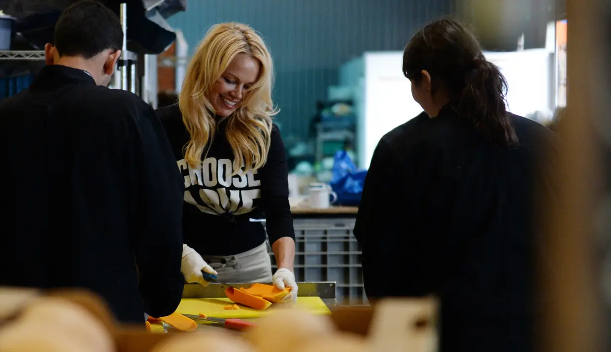 Aktris AS, Pamela Anderson memotong bahan makanan di sebuah kamp untuk imigran di Calais, Prancis, 3 Mei 2017. Pamela Anderson membantu kegiatan relawan di kamp tersebut, seperti memasak dan memilah selimut. (FRANCOIS LO PRESTI/AFP)