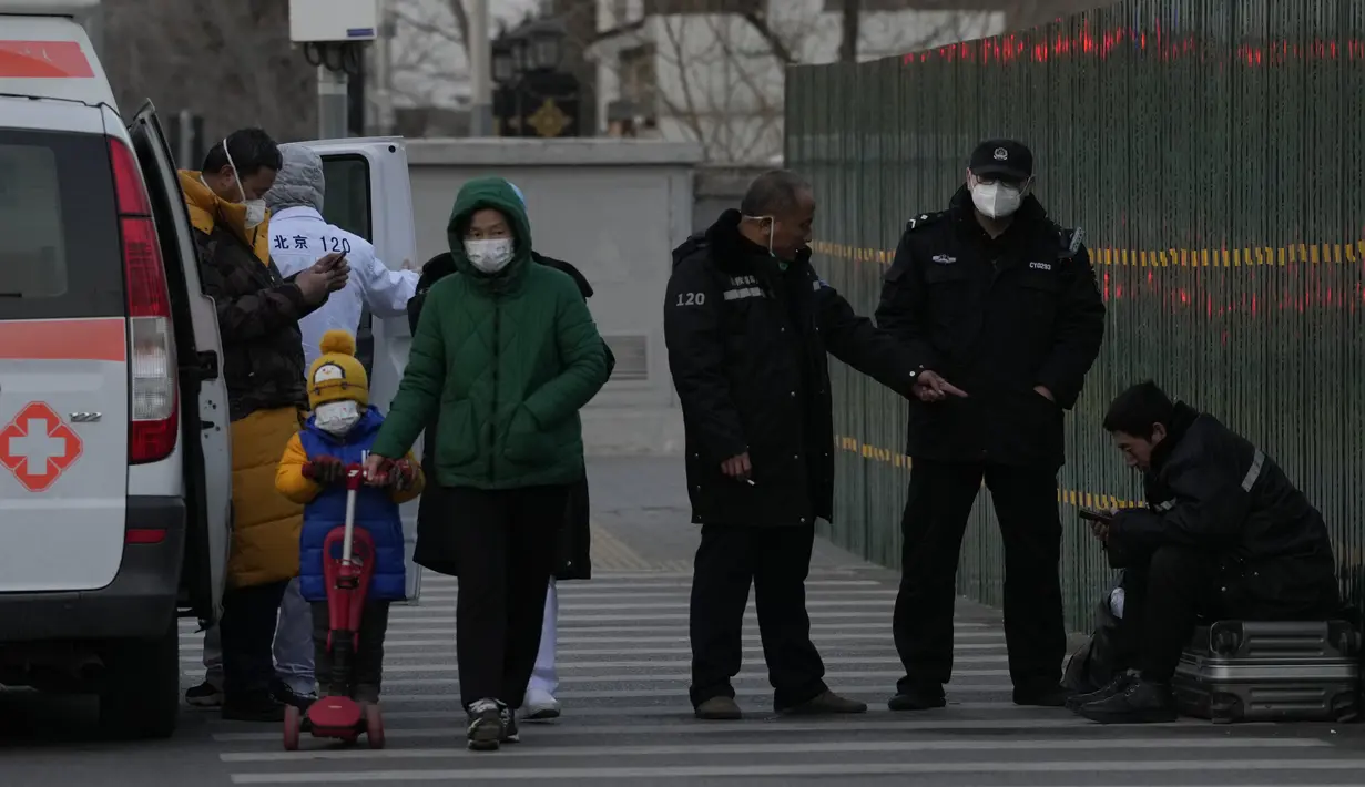 Personel polisi memeriksa seorang pria yang tampak tidak sehat dan sedang beristirahat di atas barang bawaannya di jalan Beijing, Jumat, 30 Desember 2022. China berada di jalan terjal untuk kembali ke kehidupan normal ketika warganya kembali ke sekolah, pusat perbelanjaan, dan restoran setelah berakhirnya kebijakan pembatasan paling parah di dunia diakhiri secara tiba-tiba, bahkan ketika rumah sakit dibanjiri pasien Covid-19 yang demam dan meriang parah. (AP Photo/Ng Han Guan)