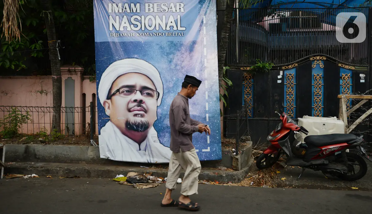 Warga berjalan di depan poster Rizieq Shihab di Jalan Petamburan 3, Jakarta, Rabu (30/12/2020). Pemerintah memutuskan untuk menghentikan kegiatan dan membubarkan organisasi massa Front Pembela Islam (FPI). (merdeka.com/Imam Buhori)