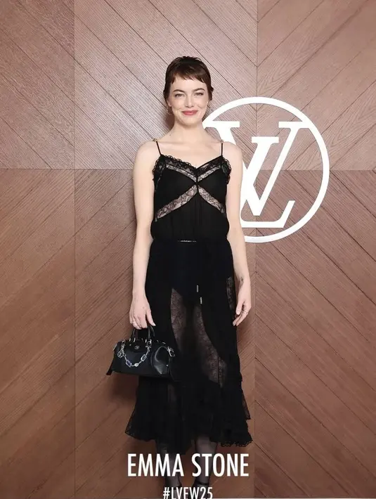 Emma Stone tampil feminim mengenakan dress lace hitam spaghetti strap. Dress ruffle tersebut dipadukan stocking sheer hitam senada dengan heels strap dan hand bagnya. [dok. Louis Vuitton]