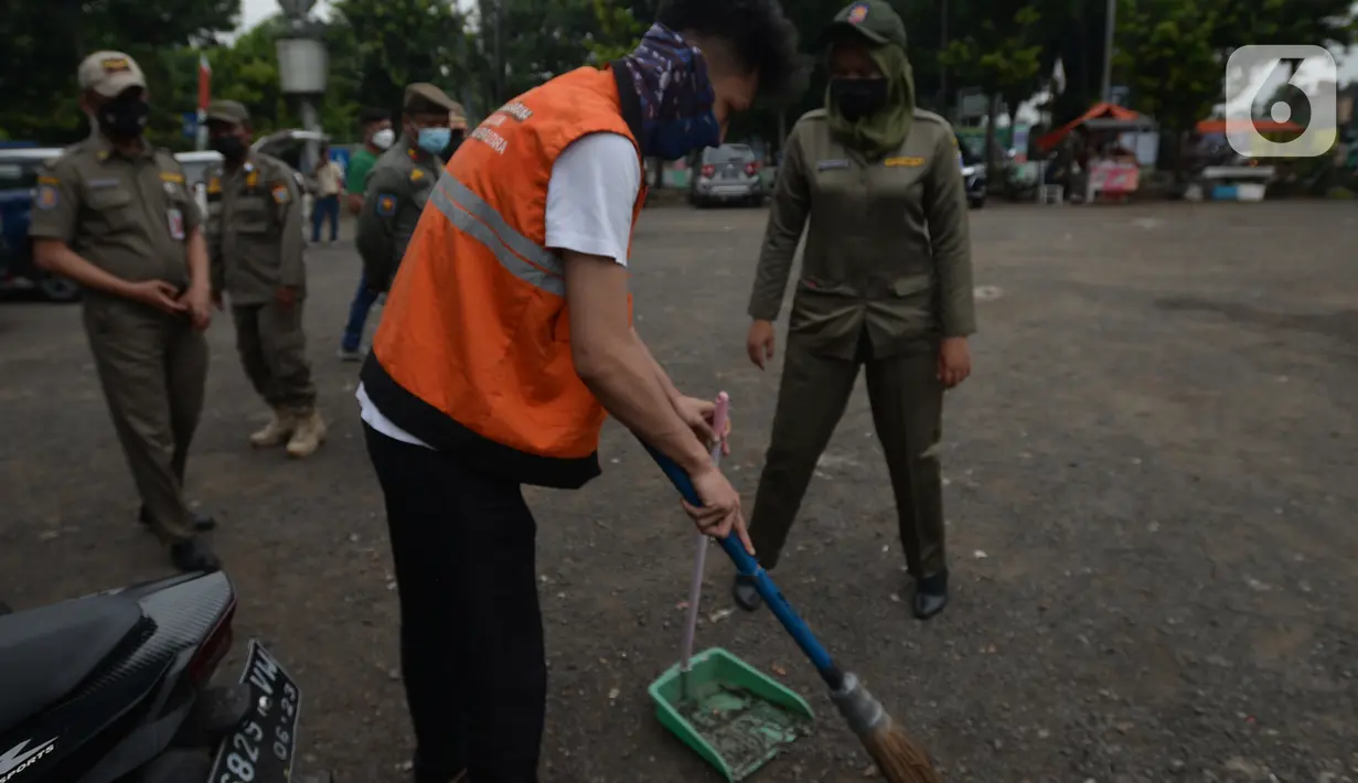 Warga yang tidak memakai masker melakukan sanksi menyapu jalan saat terjaring razia protokol kesehatan COVID-19 di Kebon Nanas, Jakarta, Selasa (15/6/2021). Saat kasus positif Covid-19 di Jakarta meningkat, masih banyak warga yang belum menjalankan protokol kesehatan. (merdeka.com/Imam Buhori)