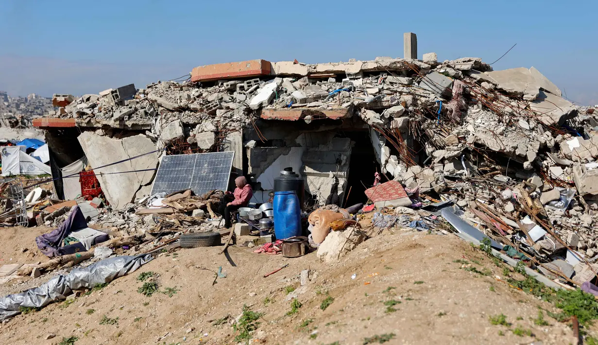 Menurut Trump, Dewan Perdamaian Gaza dirancang untuk mengawasi pembentukan pemerintahan teknokrat Palestina yang masih akan dibentuk, sekaligus memantau proses rekonstruksi di Jalur Gaza. Tampak dalam foto, para pengungsi Palestina hidup di tengah reruntuhan rumah dan bangunan yang hancur akibat serangan militer Israel selama lebih dari dua tahun di wilayah Gaza, di kamp pengungsi Jabalia, di bagian utara Jalur Gaza pada Sabtu 17 Januari 2026. (Omar AL-QATTAA/AFP)