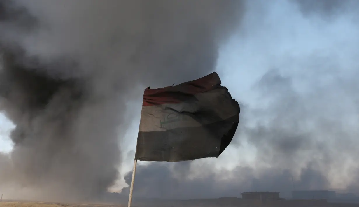Sebuah bendera Irak terlihat di depan ladang minyak yang dibakar oleh ISIS di Qayyara, selatan Mosul, Irak, (23/11).Sebelumnya, sekitar enam sumur minyak telah dibakar ISIS di kawasan tersebut. (REUTERS/Goran Tomasevic)