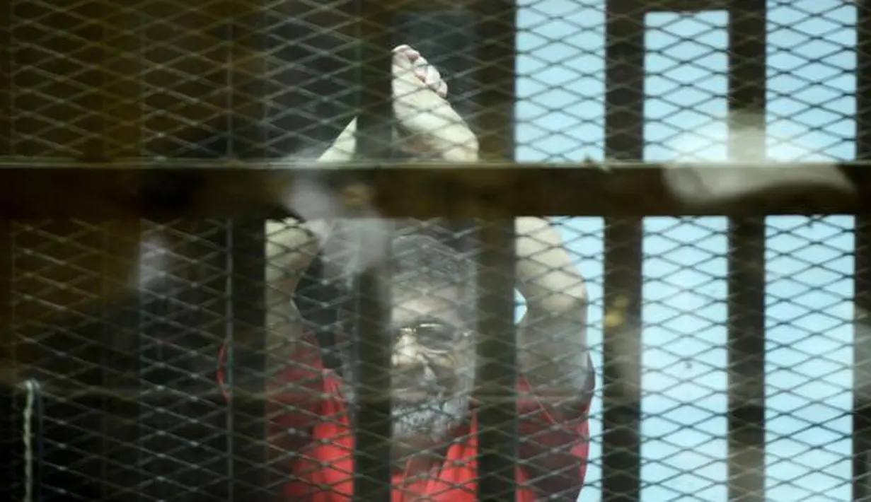 Mantan Presiden Mesir Mohammed Morsi mengenakan seragam merah saat menjalani sidang di Kairo, Mesir, 18 Juni 2016. Mohammed Morsi sesaat setelah dia berbicara dari balik sangkar kaca, tempat di mana dia ditahan selama sesi persidangan. (MOHAMED EL-SHAHED/AFP)