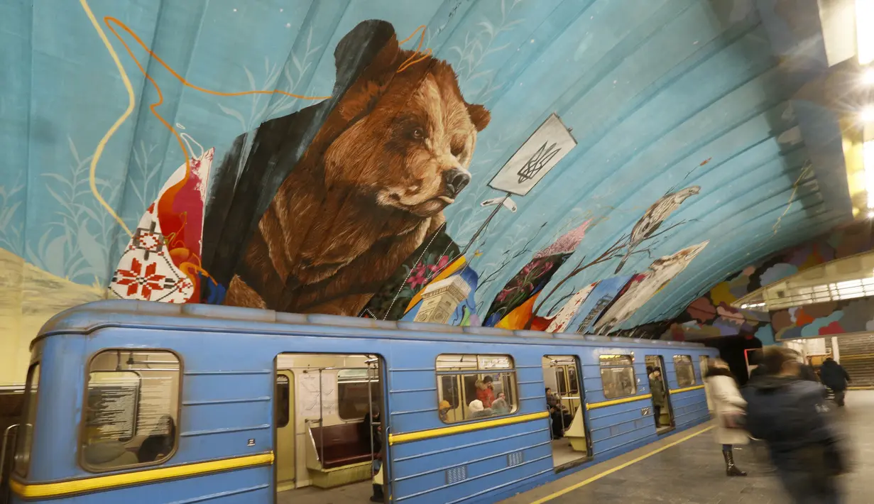 Penumpang melewati kereta di bawah mural yang menghiasi dinding stasiun metro bawah tanah kota di Kyiv, Ukraina, Rabu, (29/1/2020). (AP Photo / Efrem Lukatsky)