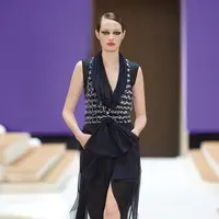 Potret busana Chanel Haute Couture Spring/Summer 2022 berikut bisa dijadikan inspirasi model baju pesta yang elegan dan mewah. Gaun warna hitam dengan detail bukaan di bagian depan ini dipadukan vest chanel berbahan tweed. Stylish dan catchy! (Dok/Chanel).