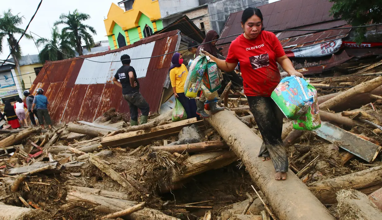 Orang-orang berjalan di atas puing-puing di daerah yang terkena banjir bandang di Masamba, Sulawesi Selatan, Rabu (15/7/2020). Banjir bandang yang terjadi akibat tingginya curah hujan itu mengakibatkan 16 orang meninggal dunia, sementara ratusan rumah rusak berat dan hilang. (AP/Khaizuran Muchtamir)