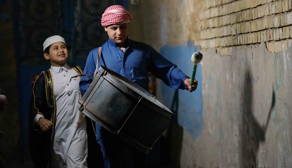 Biasanya mesaharati membawa genderang kecil (tambur) yang ditabuh secara ritmis sambil menyerukan kalimat-kalimat pengingat. Tampak dalam foto, Wissam Ali, seorang "mesaharati" atau penyeru subuh berusia 22 tahun, saat membangunkan orang-orang untuk makan sebelum matahari terbit, selama bulan suci Ramadan, di lingkungan miskin distrik Fadhil di Baghdad, Irak, Senin 23 Februari 2026. (AP Photo/Hadi Mizban)