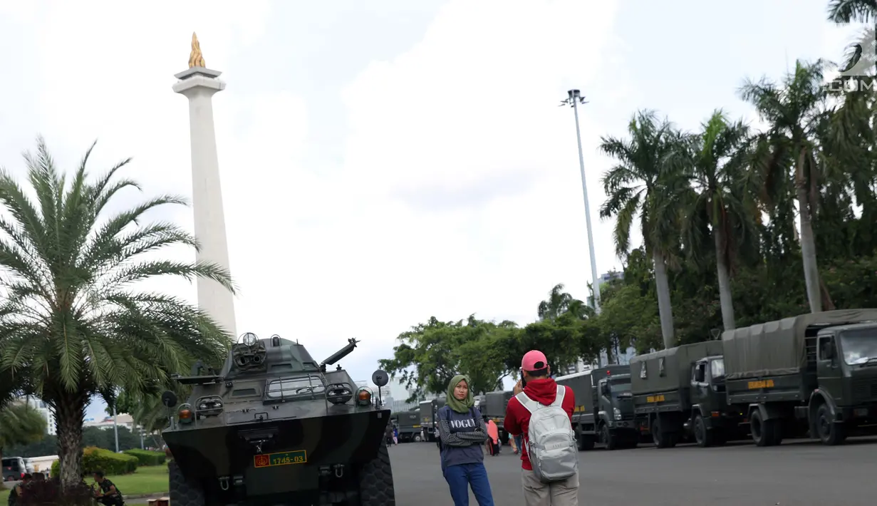 Warga berpose berlatar Tugu Monas dan kendaraan taktis TNI di kawasan Monumen Nasional, Jakarta, Jumat (19/4). Libur panjang perayaan Paskah 2019 dimanfaatkan warga untuk berwisata di kawasan Monumen Nasional. (Liputan6.com/Helmi Fithriansyah)