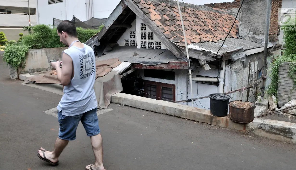 Pejalan kaki melintasi sebuah rumah usang di halaman belakang apartemen Thamrin Executive Residence, Kebon Melati, Jakarta, Minggu (22/9/2019). Rumah milik Elis (46) itu menjadi satu-satunya yang bertahan di antara gedung-gedung tinggi yang dibangun sejak 2012 silam. (merdeka.com/Iqbal S Nugroho)