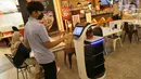 Seseorang berinteraksi dengan robot pramusaji “Bellabot” yang mengantar makanan di Tangcity Mal, Kota Tangerang, Rabu (27/10/2021). Robot karakter hewan itu melayani antar pesan makanan bagi pengunjung guna mengurangi interaksi mengingat masih dalam pandemi covid-19. (Liputan6.com/Angga Yuniar)