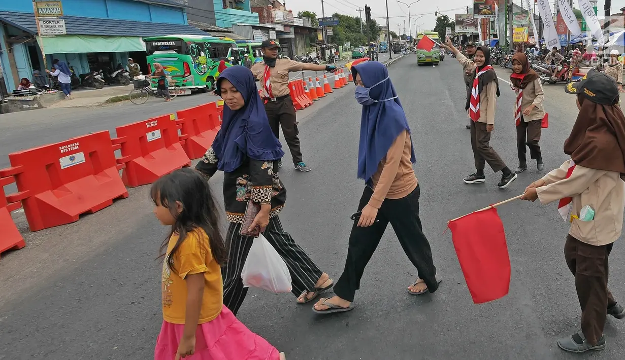 Anggota Pramuka membantu menyebrangi warga saat mengatur lalu lintas di jalur mudik kawasan pasar Surodadi, Tegal  Jawa Tengah, Senin (3/6/2019). Puluhan anggota Pramuka  membantu polisi mengatur lalu lintas selama arus mudik maupun arus balik. (Liputan6.com/Herman Zakharia)