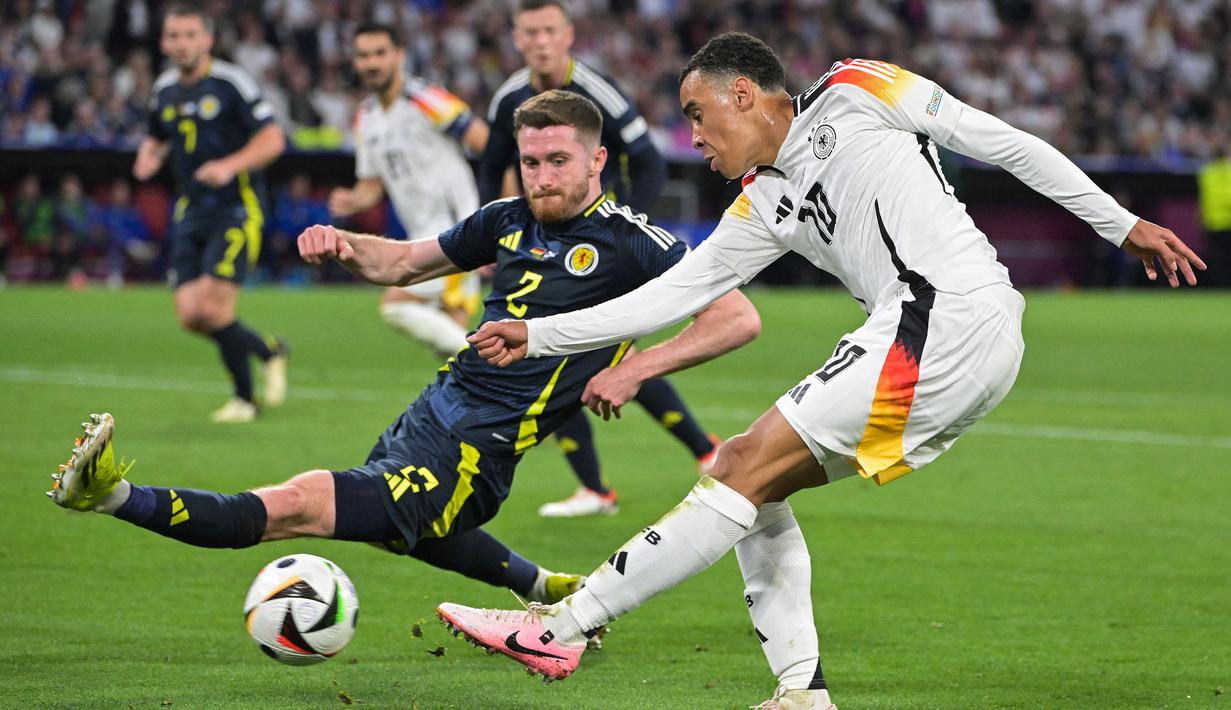 Pemain Jerman, Jamal Musiala (kanan) berusaha melakukan shooting ke gawang Skotlandia dihalangi Anthony Ralston pada laga pembuka Grup A Euro 2024 di Allianz Arena, Munchen, Jerman, Sabtu (15/06/2024) WIB. (AFP/Damien Meyer)