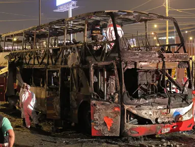 Petugas kepolisian berdiri dekat kerangka sebuah bus bertingkat yang hangus terbakar di terminal bus antarprovinsi, kota Lima, Peru, Minggu (31/3) malam. Sedikitnya 20 orang tewas dan belasan lainnya terluka dalam peristiwa nahas tersebut. (Photo by Luka GONZALES / AFP)