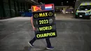 Seorang kru tim Red Bull Racing membawa papan bertuliskan Max Verstappen sebagai juara dunia Formula 1 2023 setelah Sprint Race F1 GP Qatar 2023 yang dihelat di Sirkuit Lusail, Qatar, Minggu (8/10/2023) dini hari WIB. (AFP/Ben Stansall)