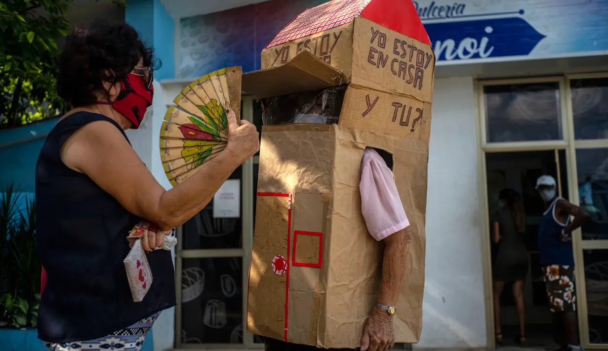 Seorang perempuan berbincang dengan pensiunan perawat bernama Feridia Rojas (82) yang memakai kotak kardus untuk melindungi dirinya dari penyebaran Covid-19 di Havana, Kuba, 8 Juli 2020. Kardus pelindung itu dilengkapi pesan yang ditulis tangan, "I'm home, and you?." (AP/Ramon Espinosa)
