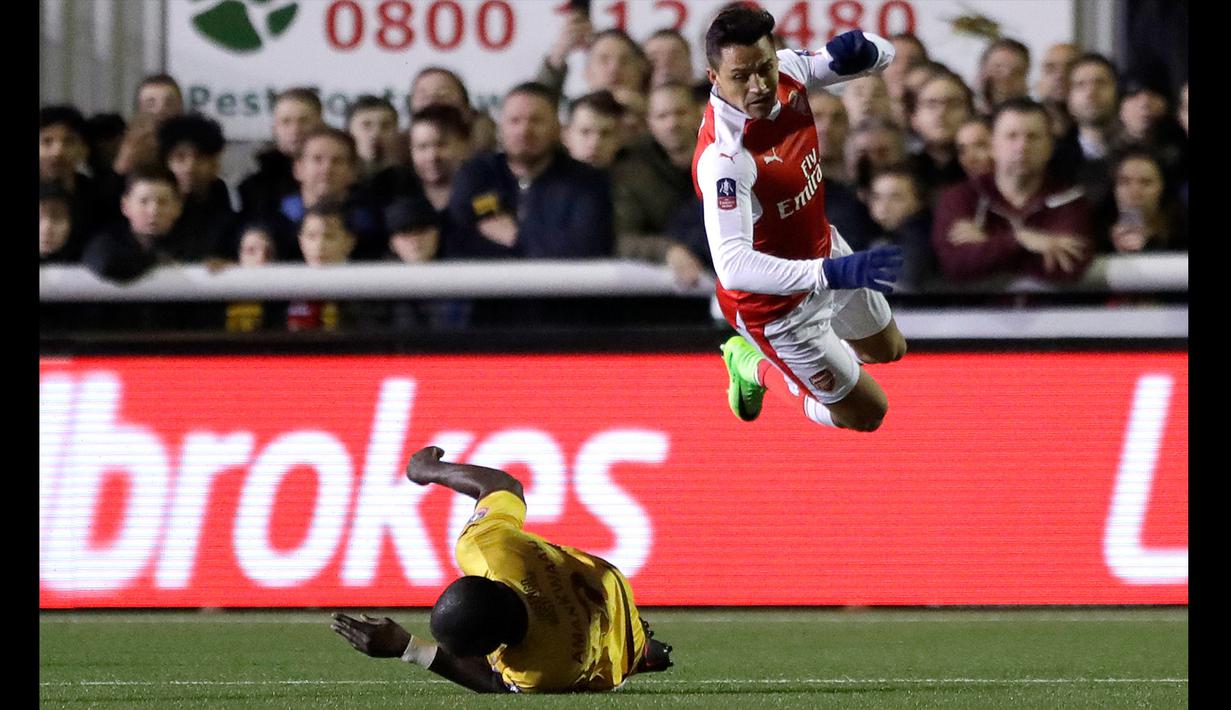 Duel pemain Arsenal, Alexis Sanchez (atas) menghindari terjangan pemain Sutton United, Kevin Amankwaah pada putaran kelima Piala FA di Gander Green Lane stadium, London; (20/2/2017). Arsenal menang 2-0. (AP/Matt Dunham)