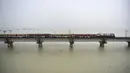 Sebuah kereta penumpang melintasi jembatan di atas Sungai Gangga yang banjir di Allahabad, India, Rabu (11/8/2021). Hujan lebat menyebabkan permukaan air Sungai Gangga dan Yamuna naik sehingga terjadi banjir. (SANJAY KANOJIA/AFP)
