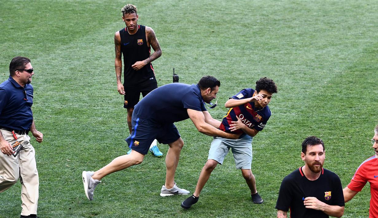 Petugas menangkap fans yang masuk ke lapangan mengejar pemain Barcelona, Lionel Messi dan Neymar saat latihan di Red Bull Arena, New Jersey, Jumat (21/7/2017). Latihan ini dilakukan jelang laga ICC 2017 melawan Juventus. (AFP/Jewel Samad)
