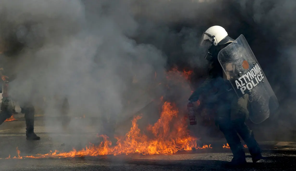 Polisi anti huru-hara saat mencoba memadamkan api dari para demonstran di Athena, Yunani, (12/11/2015). Semua aktifitas perkantoran, publik dan penerbangan ditutup karena aksi ini. (REUTERS/Michalis Karagiannis)