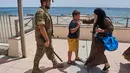 Seorang wanita berbicara dengan seorang migran berusia 12 tahun tanpa pendamping sementara seorang tentara Spanyol mengawal anak tersebut ke perbatasan Spanyol-Maroko dari wilayah kantong Spanyol di Ceuta, Senin, 3 Agustus 2026. (Foto AP/Bernat Armangue)