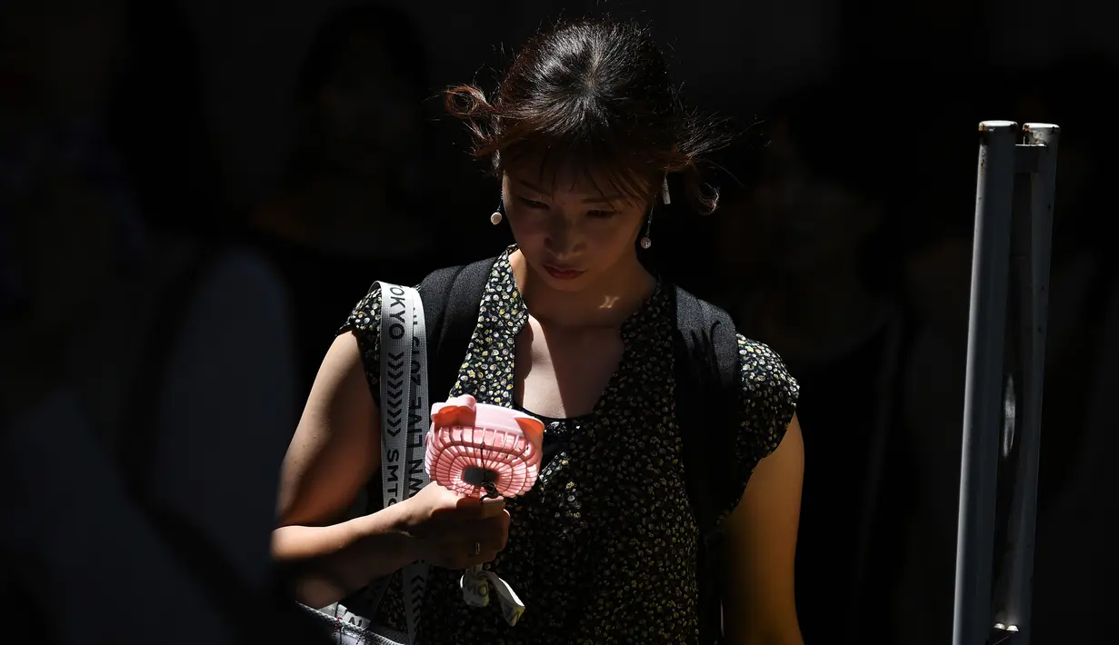 Seorang wanita memegang kipas portabel saat melintasi jalan selama gelombang panas di distrik Shin-Okubo Tokyo pada Minggu (4/8/2019). Setelah menyerang beberapa wilayah di Eropa, suhu tinggi juga terjadi di Jepang. (Charly TRIBALLEAU / AFP)