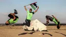 Seorang pemuda memegang bendera Palestina melompat saat menunjukkan keterampilan parkour mereka di dekat tenda warga di perbatasan Gaza, Palestina (10/4). (AFP Photo/Said Khatib)