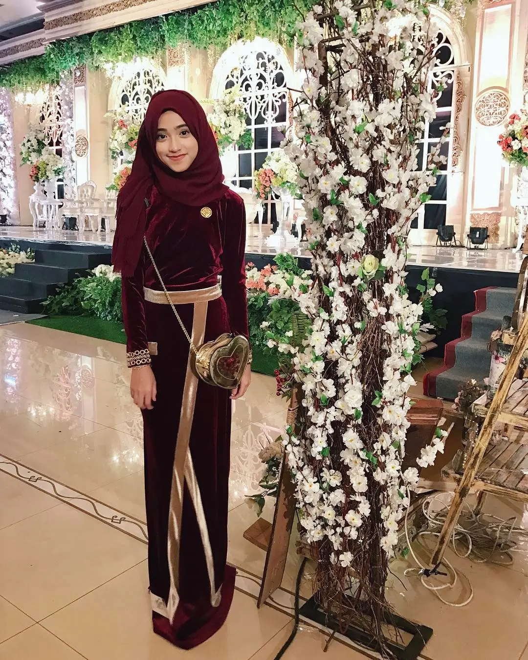 Untuk kondangan kamu bisa mengenakan long dress dengan bahan bludru berwarna merah dipadukan warna gold untuk memberikan aksen, kamu bisa samakan hijabnya sama pakaian kamu. (sumber foto: @shireeenz/instagram)